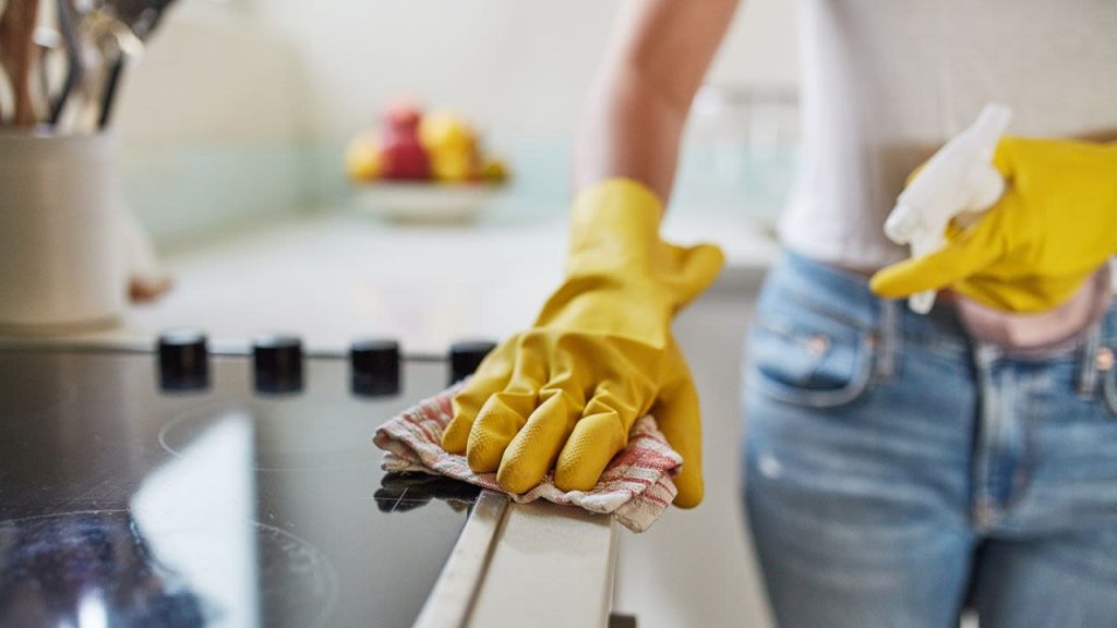 women cleaning electric stove with yellow cleaning gloves