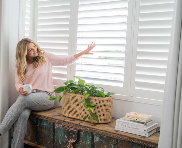 plantation shutters on a window and woman touching it 