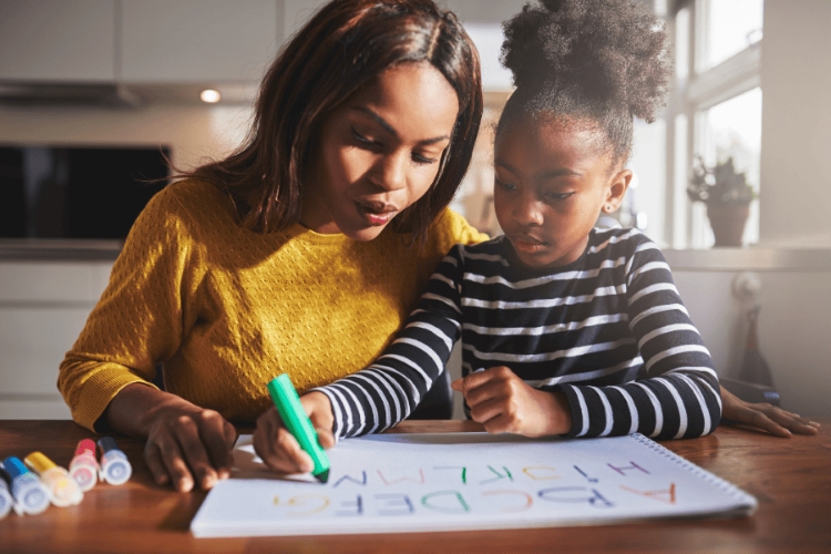 mother and daughter sitting at the table, the daughter is doing handwriting exercises