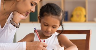 a mother watching over her daughter writing in a notebook